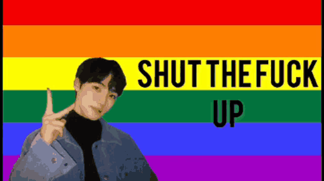 a man is standing in front of a rainbow flag with the words shut the fuck up above him
