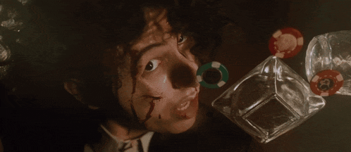 a man with blood on his face looks up at a bottle of alcohol and poker chips