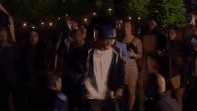 a group of young people are standing around a man in a blue hat .