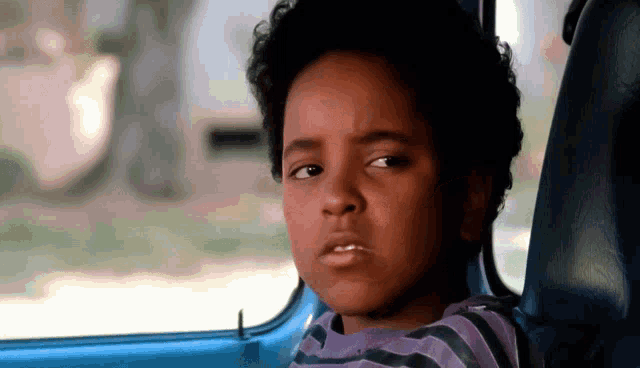 a young boy with curly hair is looking out of a blue car window