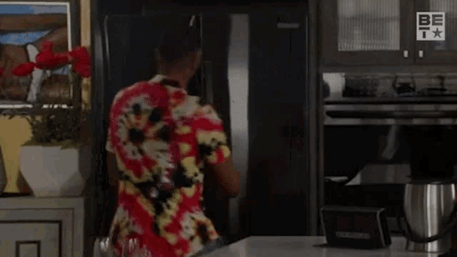 a man in a hawaiian shirt is opening a refrigerator door .