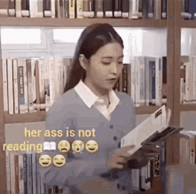 a woman is reading a book in a library while standing next to a bookshelf .