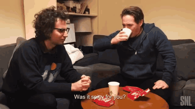 two men sit on a couch drinking coffee and one of them says " was it spicy for you ? "