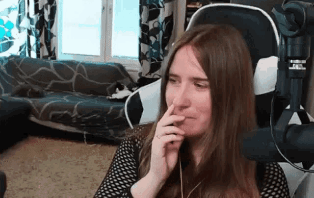a woman is sitting in a chair in front of a microphone and covering her mouth with her hand .