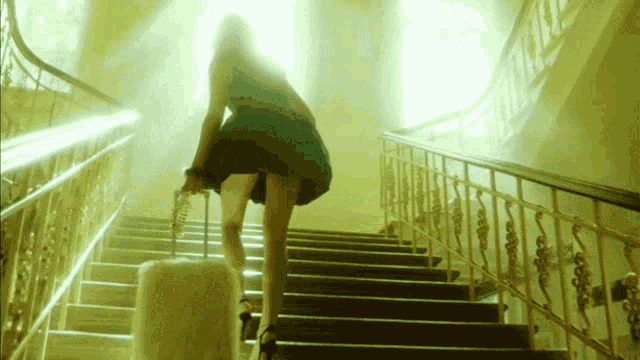 a woman in a green dress is walking up a set of stairs with a suitcase