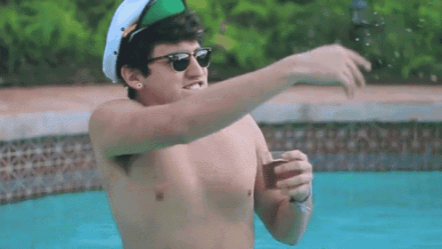 a shirtless man wearing sunglasses and a hat is standing in a pool holding a cup .