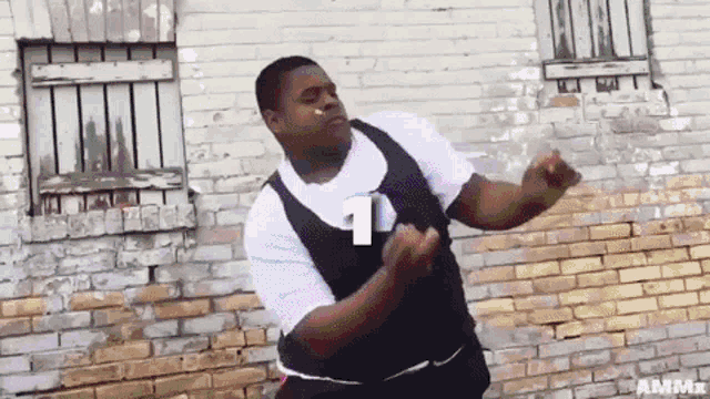 a man is dancing in front of a brick wall and has the number 1 on his shirt