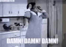 a woman in an apron is standing in a kitchen with a drink in her hand .
