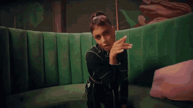 a woman is sitting on a green couch with her hand on her chin