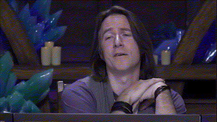 a man with long hair is sitting at a table with balloons and candles in the background .