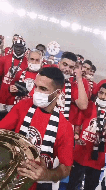 a man wearing a mask holds a trophy in front of a crowd of people