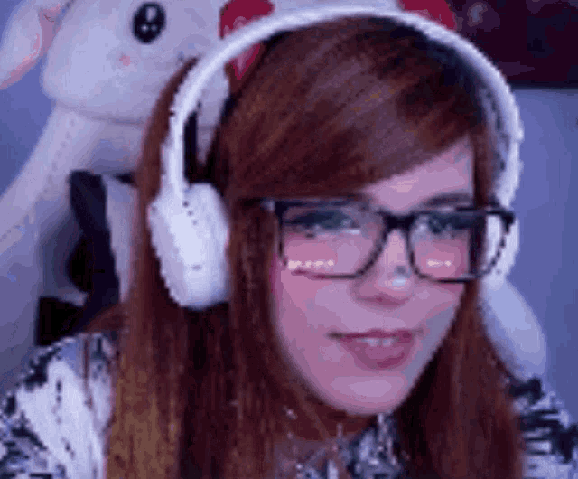 a woman wearing headphones and glasses is smiling in front of a stuffed animal .