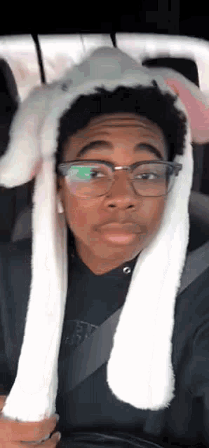 a young man wearing glasses and a bunny ear hat is sitting in a car .