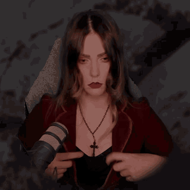 a woman wearing a black necklace with a cross on it is sitting in front of a microphone