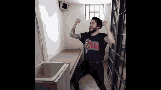a man wearing a zelda shirt is standing in a jail cell .
