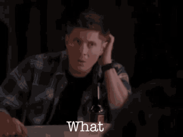 a man in a plaid shirt is sitting at a table with a bottle of wine and the words what written on the table