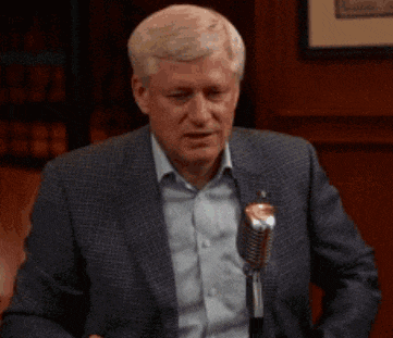 a man in a suit is talking into a microphone and pointing