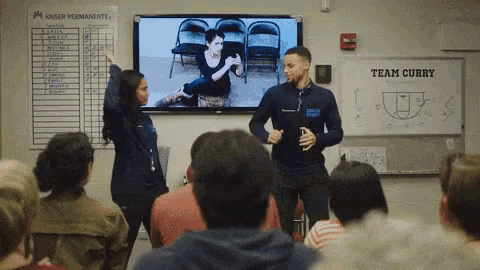 a man and a woman are standing in front of a group of people in front of a whiteboard that says team curry