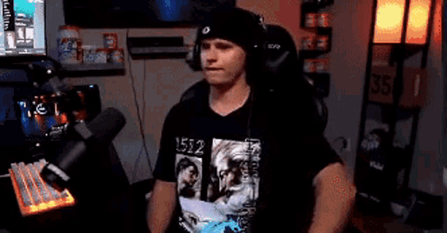a man wearing a t-shirt that says 1512 is sitting in a chair in front of a microphone .