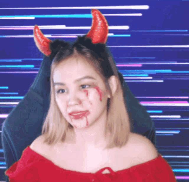a woman wearing devil horns and blood on her face is sitting in a chair