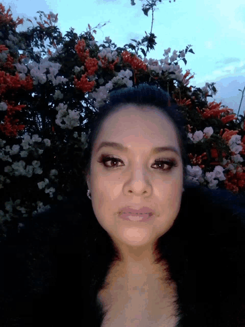 a woman stands in front of a bush with flowers