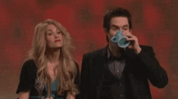 a man and a woman are standing next to each other and the man is holding a coffee cup