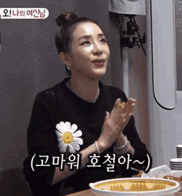 a woman wearing a black sweater with a yellow flower on it is clapping her hands