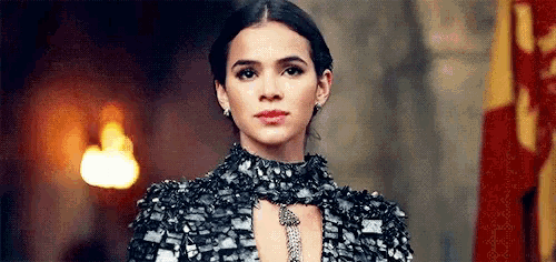 a woman in a black dress and necklace is standing in front of a flag .
