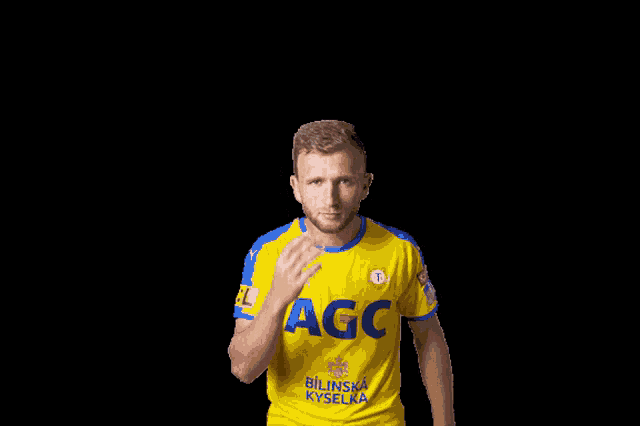 a man in a yellow and blue agc shirt scratches his head