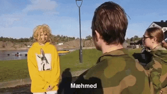 a man in a camouflage shirt is talking to a woman in a yellow sweatshirt with the name mahmed on it