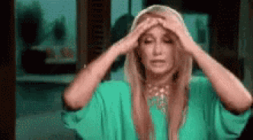 a woman in a green dress is holding her head in pain .