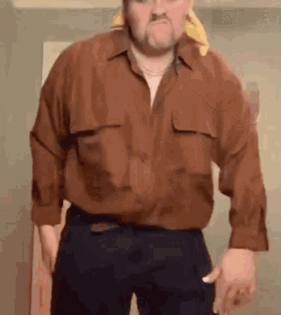 a man in a brown shirt and black pants is standing in a room with his hands in his pockets .