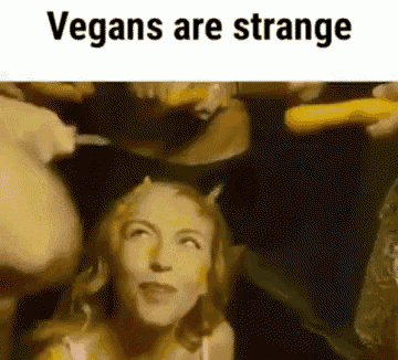 a woman with horns on her head is surrounded by a bunch of vegetables and says vegans are strange .