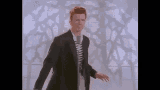 a man in a suit is dancing in front of a microphone in front of a window .