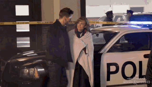 a woman wrapped in a blanket stands next to a police car