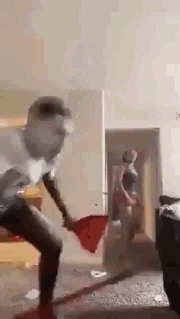 a man is holding a red towel in a living room while a woman is standing in the background .