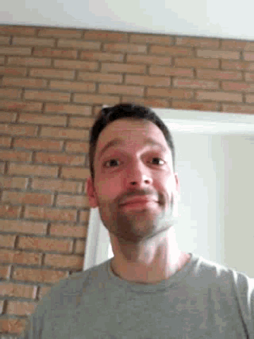 a man with a beard is standing in front of a brick wall and making a funny face .