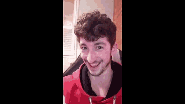 a young man with curly hair and a beard is smiling and making a funny face while sitting in a chair .