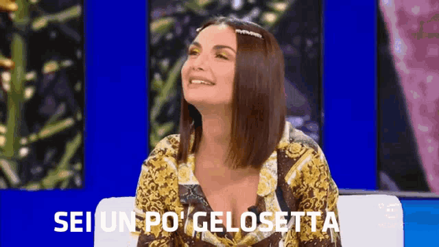 a woman is sitting on a couch and smiling with the words sei un po ' gelosetta behind her .