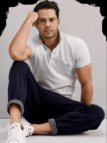 a man in a grey polo shirt sits on the floor with his hand on his chin