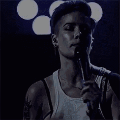 a man in a white tank top is singing into a microphone on a stage .