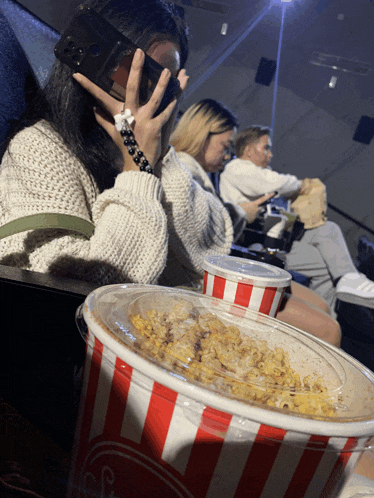 a striped bucket of popcorn sits on a table in front of a woman wearing a virtual reality headset