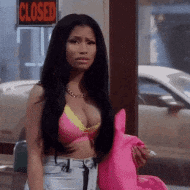 a woman in a pink bikini is holding a pink pillow in front of a closed store .