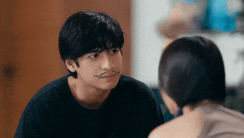 a young man with a mustache painted on his face looks at a woman
