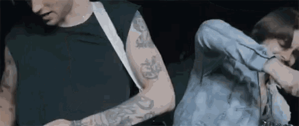a man with tattoos on his arms is playing a guitar while a woman looks on .