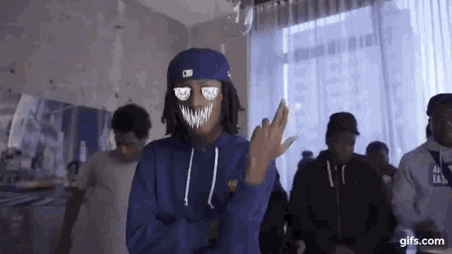a group of young men are standing in a room . one of the men is wearing a mask .
