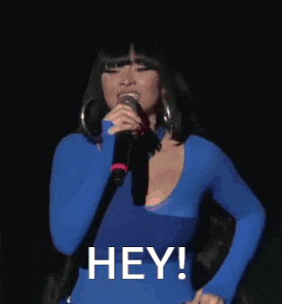 a woman in a blue shirt is singing into a microphone with the word hey written on the bottom