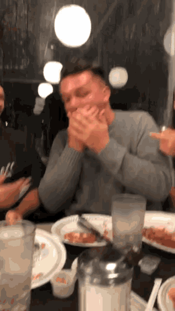 a man sitting at a table with plates of food covering his mouth with his hands