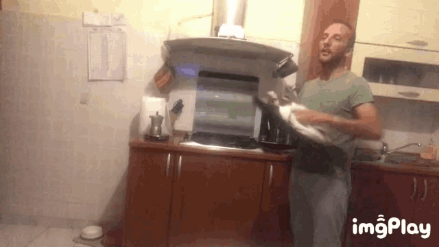 a man is holding a cat in his arms in a kitchen with imgplay written on the bottom right