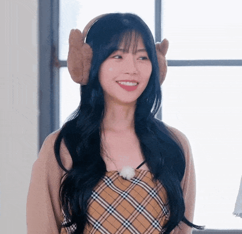 a woman wearing a plaid top and ear warmers smiles